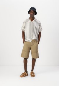 Kortærmet, stribet skjorte med knapper i beige og blå, parret med khaki cargo shorts med sidelommer og tan snørebåndssneakers.