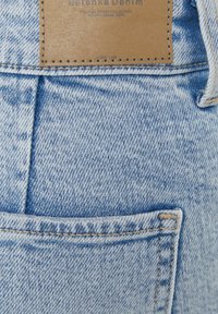 Ljusblå denimjeans med texturerad yta, med en brun läderlapp vid midjebandet och sydda fickor.