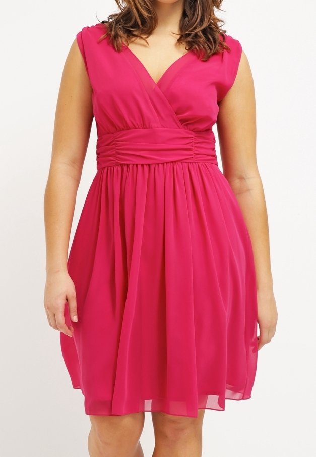 Robe rouge sans manches longueur genou avec une taille froncée et un col en V portée par une personne debout, sur un fond clair uni.