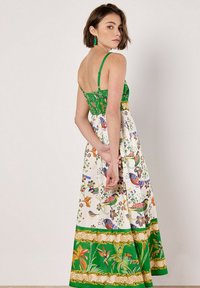 Abito maxi con corpetto verde e gonna bianca a fantasia floreale. Presenta spalline sottili, schiena arricciata e intricate decorazioni con uccelli tropicali.