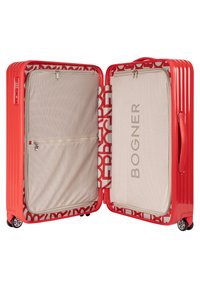 Maleta dura roja con un exterior ranurado. El interior cuenta con compartimentos de malla beige, un forro de marca y bolsillos con cremallera para una mejor organización.