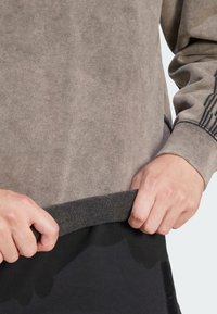 Pullover-tröja i dämpad grå färg med en mjuk textur. Har en mörk ribbad nederkant, och händer justerar nederkanten.