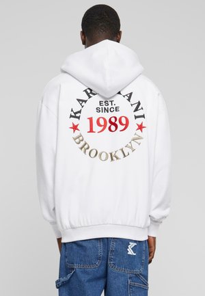 White hooded sweatshirt featuring "KARL KANI BROOKLYN EST. SINCE 1989" printed in black, red, and gold, with a relaxed fit and ribbed hem.