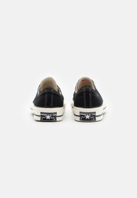 Svarte lavtoppsko i lerret med hvite gummisåler, med kontraststing og klassisk Converse All Star-merke på hælen.