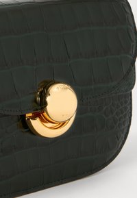 Green crocodile-embossed leather bag with a rounded gold clasp and stitched edges. Features a flap closure and a smooth, glossy texture.