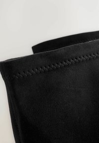 Schwarzer Wildlederstoff mit einer glatten Textur und kontrastierenden Nähten entlang der oberen Kante, der ein minimalistisches Design zeigt.