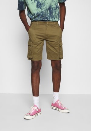 Pantalones cortos de cargo en verde oliva con múltiples bolsillos laterales, combinados con una camiseta de patrón tie-dye y zapatillas rosas. Tela de algodón, diseño casual.