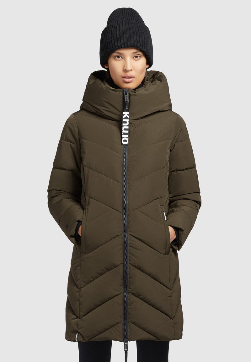 Olijfgroen pufferjas met een ritssluiting, chevronpatroon en grote capuchon. Heeft een logo aan de voorkant en zijzakken. Inclusief zwarte gebreide beanie.