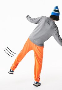 Sweat-shirt gris avec texte noir au dos, assorti à un pantalon en velours orange vif et des baskets noires avec des accents bleus.