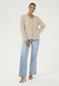 Beige blouse with black polka dots, ruffled front, long sleeves, and a v-neckline, paired with light blue wide-leg jeans and beige heels.