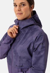 Lila Vaude-Jacke mit durchgehendem Reißverschluss, verstellbarer Kapuze, elastischen Bündchen und dem Markenlogo auf der unteren linken Seite. Glatte Textur.