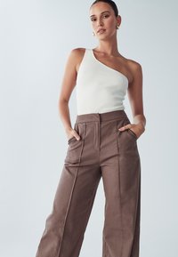 Biały prążkowany top na jedno ramię połączony z brązowymi szerokimi spodniami z bocznymi kieszeniami i gładką fakturą.