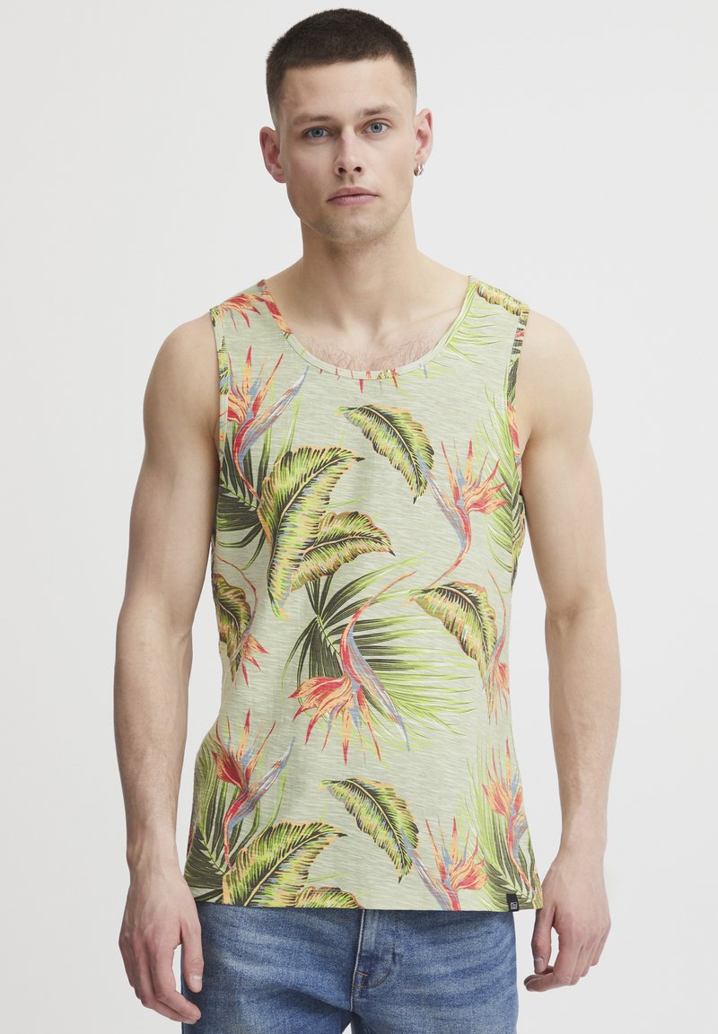 Lysegrønn tanktop med et livlig mønster av tropiske blader og blomster. Myk stoff, rund halslinning og avslappet passform. Bæres med blå jeans.