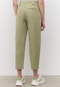 Lichtgroene, cropped broek met een gladde textuur, voorzien van een achterzak met knoopdetail, gecombineerd met witte sneakers.