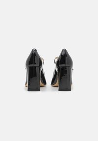 Chaussures à talons hauts en cuir verni noir avec un talon épais et un dos pointu. Texture lisse avec une finition brillante et des côtés ouverts.