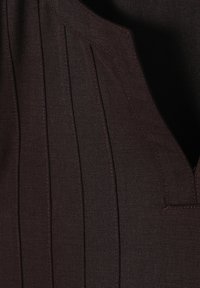 Haut en tissu brun foncé présentant des plis verticaux et un col en V. La texture est lisse avec des accents de coutures visibles.