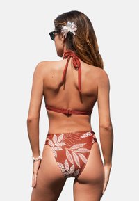 Bikini de dos piezas en color óxido con patrones de hojas blancos; diseño de cuello halter, parte inferior de talle alto y textura suave.