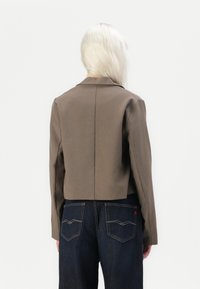 Brun cropped jakke med klassisk krage, med lange ermer og rett bakdesign, kombinert med mørkeblå denimbukser.