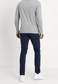 Šedé tričko s dlouhým rukávem a tmavě modré kalhoty z měkké látky, přiléhavý střih, doplněné bílými teniskami. Bez viditelných vzorů či doplňků.