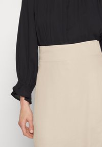 Blusa preta de mangas longas e pregas, combinada com uma saia alta de cor creme. Textura suave, ajuste acentuado e detalhes de mangas franzidas.