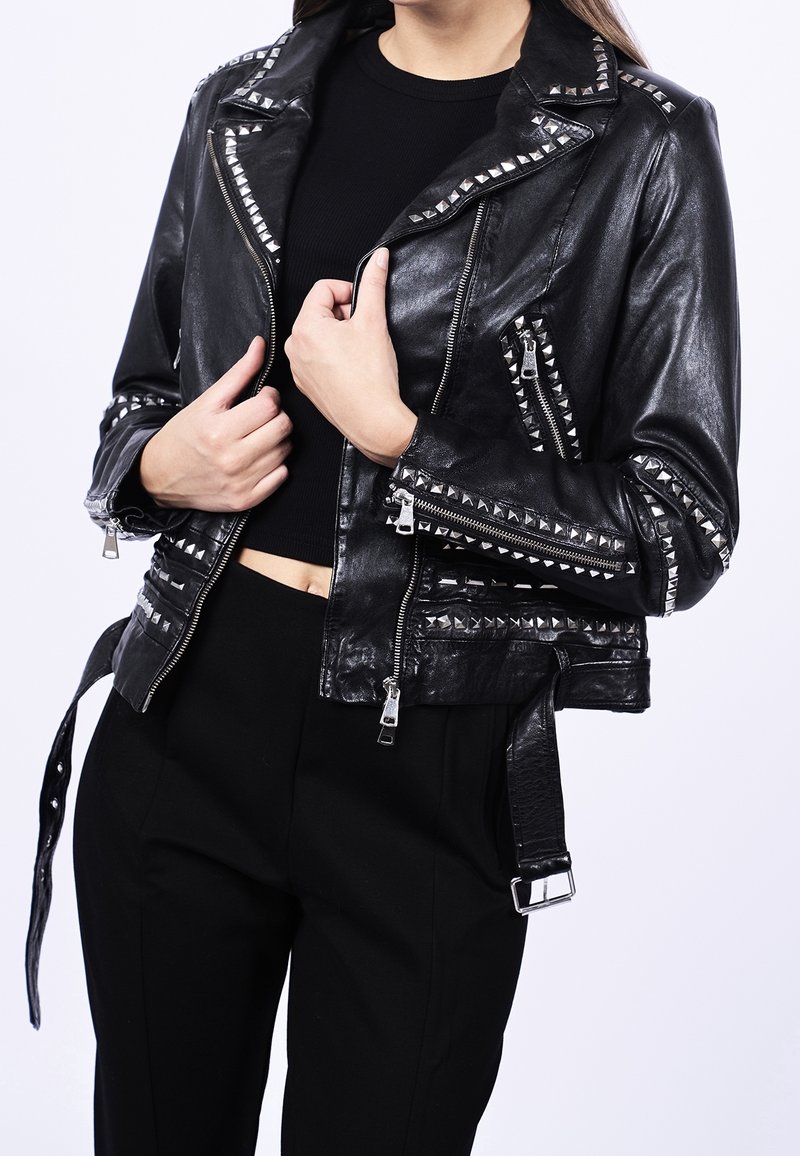 Veste de motard en cuir noir avec des clous argentés, des poches à fermeture éclair et une taille ceinturée. Caractérisée par un style court et une finition texturée.