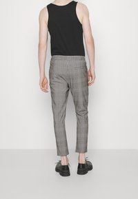 Zwarte tanktop gecombineerd met grijs broek met ruitpatroon. De broek heeft een slim fit en wordt aangevuld met zwarte veterschoenen.