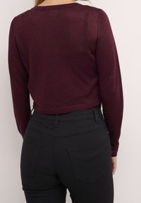 Bordeaux lange mouw top met een cropped ontwerp en subtiele glans, gecombineerd met hoge taille zwarte jeans met achterzakken.
