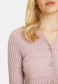 Jasnoróżowy kardigan prążkowany z dekoltem w serek i zapięciem na perłowe guziki, z teksturowanymi pionowymi paskami i dopasowanym krojem.
