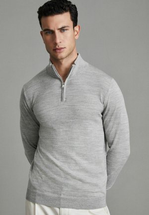 Grå zip-neck tröja med en slät textur och subtilt tonat mönster. Långa ärmar och en figurnära design förstärker den moderna stilen.