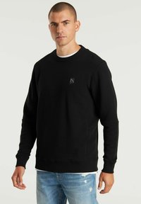 Schwarzer, strukturiertes Sweatshirt mit geripptem Rundhalsausschnitt und dezentem Logo. Kombiniert mit hellblauen, ausgewaschenen Jeans für einen Kontrast.