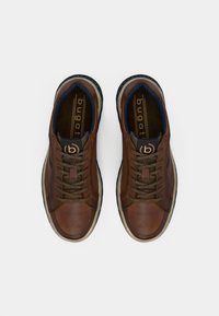 Pruunid nahast tossud ümara nina, paelaga kinnitusega, tekstureeritud pinnaga ning kontrastsete tumesiniste detailidega sees ja tallal.