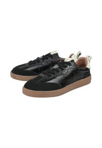 Sneakers neri con una combinazione di pelle verniciata e texture scamosciata, dotati di spessi lacci neri, dettagli crema e suola in gomma marrone.