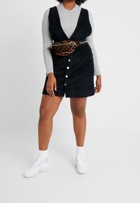 Schwarzes Corduroykleid mit tiefem V-Ausschnitt, Knopfleiste und passender Leoprint-Gürteltasche. Trägt man mit einem taillierten grauen Pullover und weißen Sneakers.