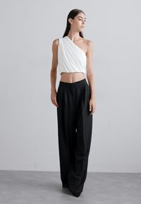 Hvit drapert en-skulder crop top kombinert med høy midje svart bredbukse. Glatt stoff, minimalistisk design og nøytrale farger.