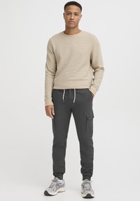 Beige texturerad långärmad topp som matchas med mörkgrå cargojoggers med elastiska manschetter och sidfickor, kompletterad med grå sneakers.
