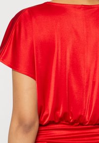 Rød satin top med løs pasform, korte ærmer, en rynket talje og glat, blank tekstur. Ingen bemærkelsesværdige mønstre eller detaljer.