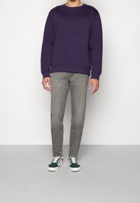 Sudadera morada con cuello redondo, combinada con jeans gris claro y zapatillas verde y blanca. El material parece suave y casual.