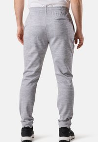 Helle graue Jogginghosen aus weichem, strukturiertem Stoff mit elastischem Bund, schlankem Schnitt und einer diskreten Gesäßtasche; kombiniert mit schwarzen Sneakers.