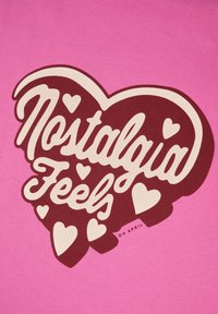 T-shirt di cotone rosa con una grande grafica a forma di cuore marrone e la scritta "Nostalgia Feels" in crema, arricchita da piccoli cuori.