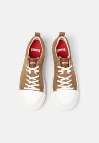 Zapatillas de ante marrón con puntera de goma blanca, cordones y entresuela. Plantilla roja con el logotipo "CAMPER". Diseño minimalista, forma redondeada.