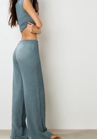 Haut court ajusté côtelé couleur sarcelle et pantalon ample à jambes larges de la même couleur, en tissu texturé ; mannequin présenté de profil sur un fond neutre.