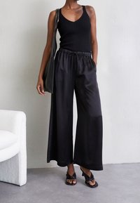 Svart ribbad linne i kombination med vida satängbyxor i svart, med elastisk midja och dragsko. Sandaler med vriden design.