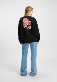Felpa nera con grafica vivace colorata e rosa sul retro, che presenta vari oggetti. Vestibilità comoda, stile casual, tessuto testurizzato.