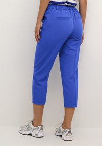 Blaue, abgeschnittene Hosen mit einem elastischen Bund. Hergestellt aus glattem Material, mit zwei Gesäßtaschen und einer bequemen Passform.