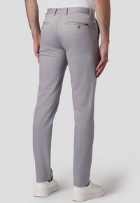 Jasnoszare spodnie w dopasowanym kroju, z tylnymi kieszeniami zapinanymi na guziki i gładkim wykończeniem tekstylnym. Noszone z białymi sneakersami.