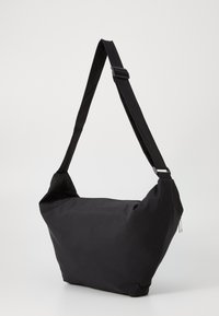 Saco preto de ombro feito de tecido suave, com uma alça ajustável, fecho com zip e um contorno relaxado com um design minimalista.