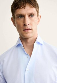 Chemise boutonnée bleu clair avec col et texture de tissu délicate ; présente une finition lisse et une coupe décontractée.