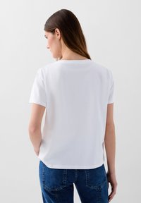 T-shirt bianca in cotone con collo rotondo e maniche corte, caratterizzata da una vestibilità ampia e un orlo dritto. Nessun motivo o accentuazione visibile.