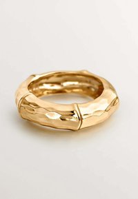 Anillo de tono dorado martillado con un diseño parecido al bambú, que presenta superficies texturizadas y lisas, forma redondeada y segmentos distintivos.