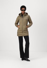 Olivroheline täispadjakate, millel on kapuuts, millel on vertikaalsed õmblused, tõmblukuga sulgemine ja küljetaskud. Kannab mustade flareerivate pükstega ja saapadega.